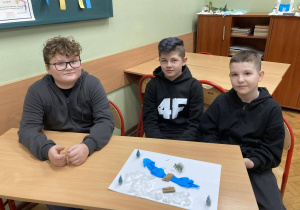 Uczniowie klasy piątej pokazują makietę Narnii z rzeką i zaśnieżonym krajobrazem wykonanym z materiałów plastycznych.