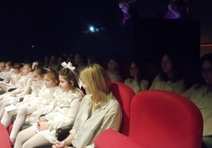 Uczennice klasy 2b w białych strojach aniołów siedzą na widowni przed występem podczas akcji Aniołkowe Granie.