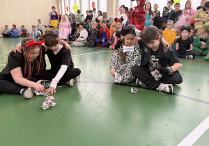 Dwoje dzieci siedzi na podłodze sali gimnastycznej i zgniata gazety podczas konkursu.