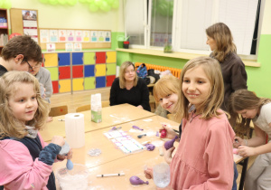 Grupa dzieci pracuje przy stoliku nad doświadczeniem, używając pojemników i materiałów plastycznych.