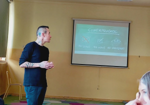 Marcin Józefaciuk prowadzi prelekcję dla uczniów w klasie; na ekranie widoczna jest prezentacja dotycząca hejtu.