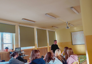 Marcin Józefaciuk stoi obok ekranu z napisem „Cyberprzemoc” podczas spotkania z uczniami.