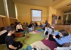 Uczniowie siedzą w kręgu na dywanie w świetlicy podczas zajęć o emocjach i depresji.