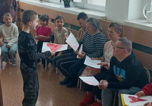 Dziecko wręcza rysunek serca osobie dorosłej podczas zajęć integracyjnych w klasie.