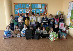 Grupa uczniów siedzi i stoi z różnymi przedmiotami zamiast plecaków, m.in. walizkami i torbami.
