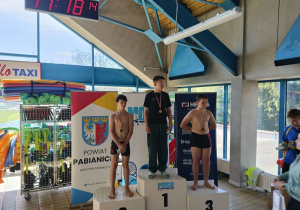 Trzech uczniów stoi na podium i prezentuje medale zdobyte w zawodach pływackich.
