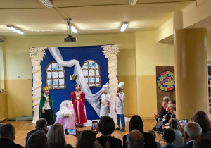 Dzieci w kostiumach odgrywają scenę z bajki „Śpiąca Królewna” przed zgromadzonymi rodzicami.