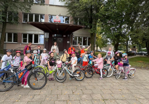 Klasa 2b z SP13 w Pabianicach z rowerami i w kaskach przed budynkiem szkoły. Grupa przygotowuje się do wycieczki rowerowej, w tle drzewa i szkolny budynek.