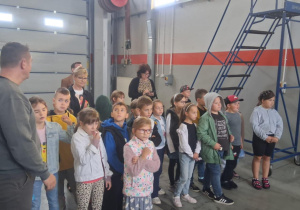 Uczniowie klasy 2b SP13 słuchają przewodnika w hali MZK. W tle nauczyciele i niebieska drabina techniczna.