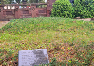 Kwatera grobowa rodziny Enderów na cmentarzu ewangelickim w Pabianicach, w tle rzeźba kobiety i czerwony pomnik, na przodzie czarna tablica z opisem.