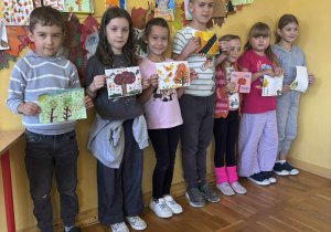 Dzieci prezentujące swoje jesienne kartki podczas konkursu w świetlicy.