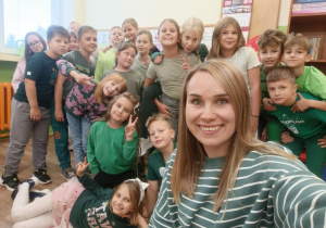 Uczniowie klasy 3B wraz z wychowawczynią Katarzyną Szczepaniak pozują do selfie ubrani w zielone stroje w ramach szkolnego „Dnia Koloru”. W tle wnętrze klasy.