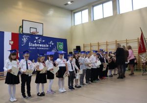 Uczniowie klas pierwszych odbierają dyplomy ślubowania od dyrekcji szkoły.