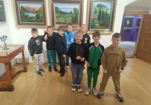 Grupa ośmiu uczniów stojących w muzeum na tle obrazów przedstawiających krajobrazy.