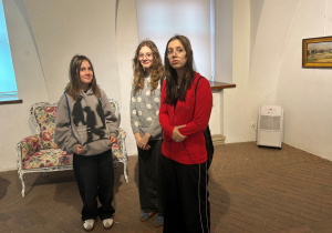 Trzy uczennice klasy 7a stoją w muzealnej sali podczas zwiedzania wystawy „Kisling w Pabianicach”. W tle widoczna stylizowana sofa w kwiatowy wzór oraz obrazy prezentowane na ścianach.