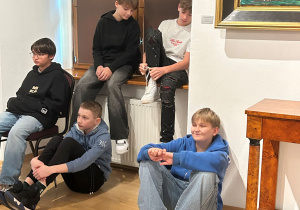 Chłopcy z klasy 7a siedzą swobodnie w sali muzeum po prelekcji podczas wystawy Kislinga w Pabianicach.