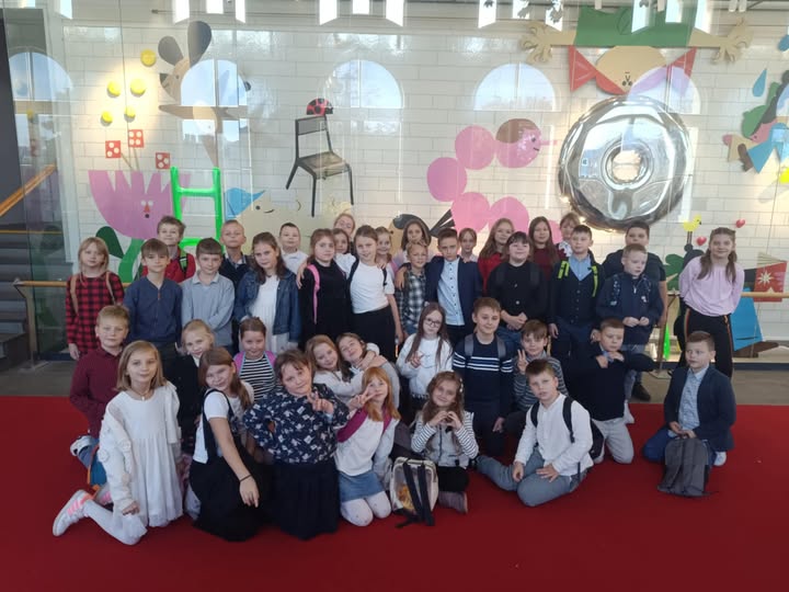 Uczniowie klas 3a i 3b pozują wsp&oacute;lnie do zdjęcia na tle kolorowej, bajkowej dekoracji w Teatrze Arlekin.