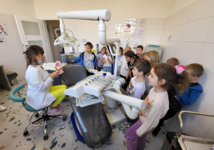 Uczniowie klasy 1b stoją przy fotelu dentystycznym i słuchają pani stomatolog.