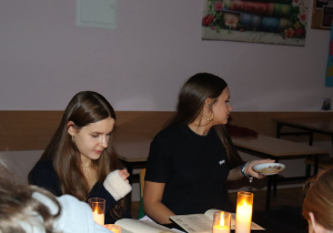 Ala i Iga z klasy 7a biorą udział w wieczornym czytaniu „Dziadów”, siedząc przy stole oświetlonym świecami.