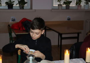 Peter z klasy 7b siedzi przy świecach podczas czytania „Dziadów” i trzyma talerzyk z ziarnami jako element obrzędu.