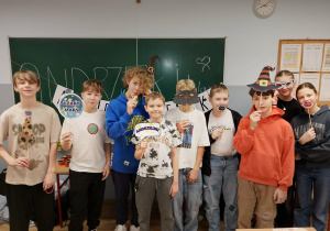 Grupa uczniów 6a i 6b pozuje z andrzejkowymi rekwizytami przed tablicą z napisem „ANDRZEJKI”.