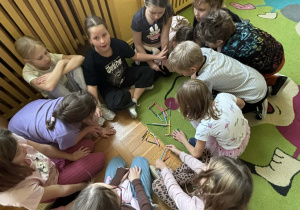 Dzieci siedzą w kręgu na dywanie i układają z kolorowych kredek różne kształty, ćwicząc współpracę podczas świetlicowego Dnia Kredki.