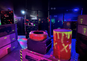 Półmroczna arena Laser Games z podświetlonymi przeszkodami i neonowymi wzorami przygotowana do rozgrywki uczniów klasy 7a.