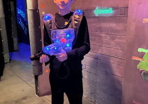 Uczeń 7a w kamizelce laserowej stoi na arenie Laser Games i trzyma pistolet, gotowy do gry.