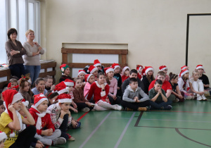 Uczniowie obserwują mikołajkowy program na sali gimnastycznej; obok nauczycielki SP 13.