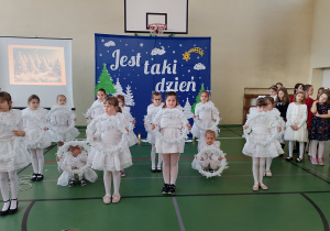 Uczennice klas młodszych w białych strojach prezentują taniec z wiankami podczas koncertu świątecznego.