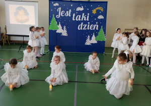 Uczennice w białych strojach wykonują taniec ze świecami podczas koncertu świątecznego na sali gimnastycznej.