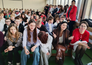 Uczniowie klas 4–8 oraz nauczyciele siedzą na ławkach w sali gimnastycznej podczas koncertu świątecznego.