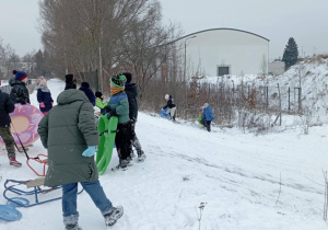 Uczniowie klasy 2b wchodzą na górkę z sankami i jabłuszkami podczas zimowej zabawy.