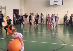 Uczniowie i nauczyciele pokonują tor na piłkach do skakania w sali gimnastycznej.