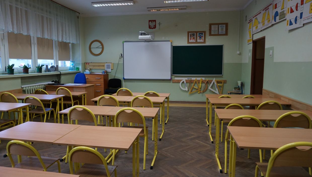 Sala matematyczna. Sala lekcyjna z ż&oacute;łtymi krzesłami, tablicą i przyrządami geometrycznymi na ścianie.
