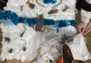 Makieta Narnii z rzeką, mostkiem i wieżą otoczona ośnieżonym krajobrazem wykonanym z materiałów plastycznych.