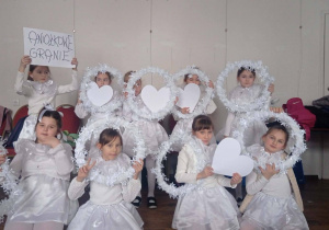Uczennice klasy 2b w strojach aniołów trzymają białe serca i obręcze oraz kartkę z napisem Aniołkowe Granie.