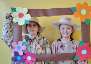 Dziewczynki w kapeluszach pozują w ozdobnej ramce podczas zajęć związanych z Dniem Babci i Dziadka.
