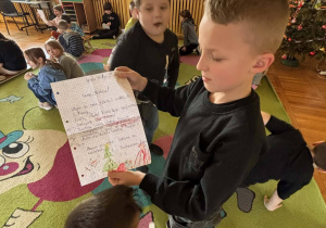 Chłopiec w świetlicy trzyma i pokazuje list otrzymany w ramach projektu „Dzieci Listy Piszą”, a wokół siedzą inne dzieci czytające swoją korespondencję.