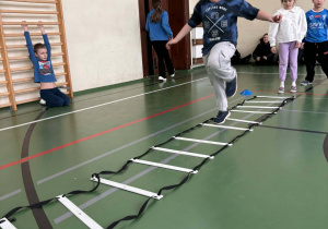 Uczeń pokonuje drabinkę koordynacyjną podczas styczniowej olimpiady sportowej świetliczaków w sali gimnastycznej.