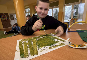 Uczeń maluje drewniany karmnik podczas styczniowych zajęć o pomaganiu ptakom zimą.