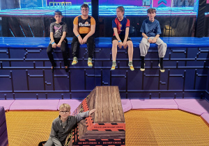 Grupa uczniów wraz z opiekunami stoi przed kolorową karuzelą w parku Hopa Lupa. To pamiątkowe zdjęcie rozpoczynające dzień pełen ruchu, integracji i wspólnej zabawy poza murami szkoły.