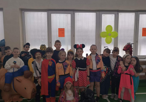 Grupa dzieci w różnorodnych kostiumach stoi razem w sali gimnastycznej i pozuje do zdjęcia.