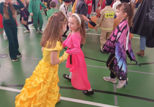 Dzieci w przebraniach karnawałowych tańczą w parach w sali gimnastycznej.
