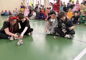 Dwoje dzieci siedzi na podłodze sali gimnastycznej i zgniata gazety podczas konkursu.