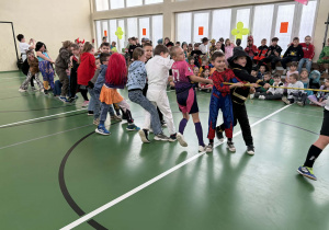 Dzieci w kostiumach karnawałowych przeciągają linę podczas konkursu w sali gimnastycznej.