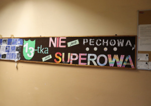 Tablica na korytarzu z napisem „13-tka jest superowa” wykonanym z kolorowych liter.