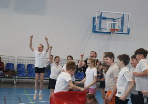 Grupa uczniów cieszy się po zakończonej konkurencji sportowej w hali.