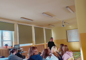 Marcin Józefaciuk stoi obok ekranu z napisem „Cyberprzemoc” podczas spotkania z uczniami.