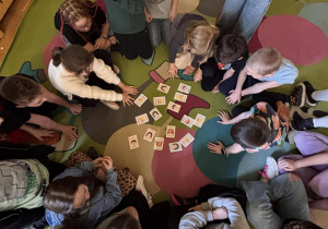 Uczniowie siedzą w kręgu wokół kart z emocjami podczas zajęć w świetlicy.